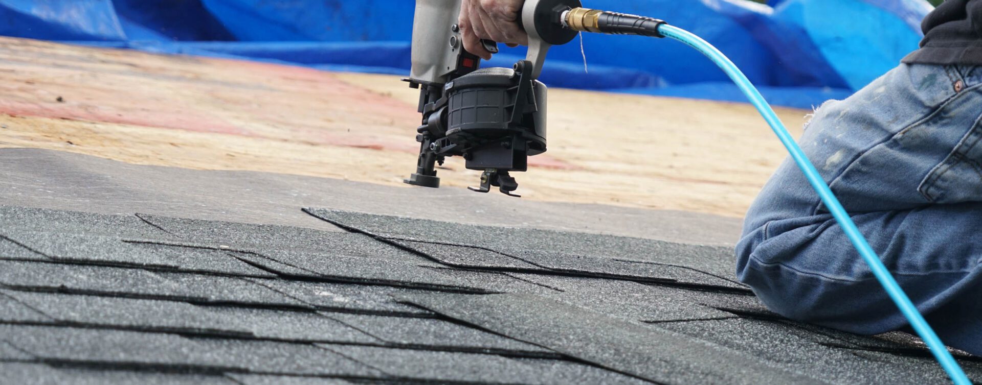 A person is using an air gun to fix the shingles.